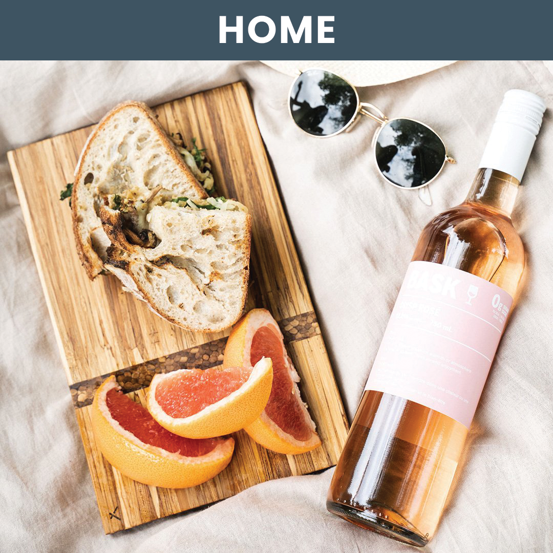 Lifestyle image of a charcuterie board surrounded by fruit, a sandwich and bottle of wine