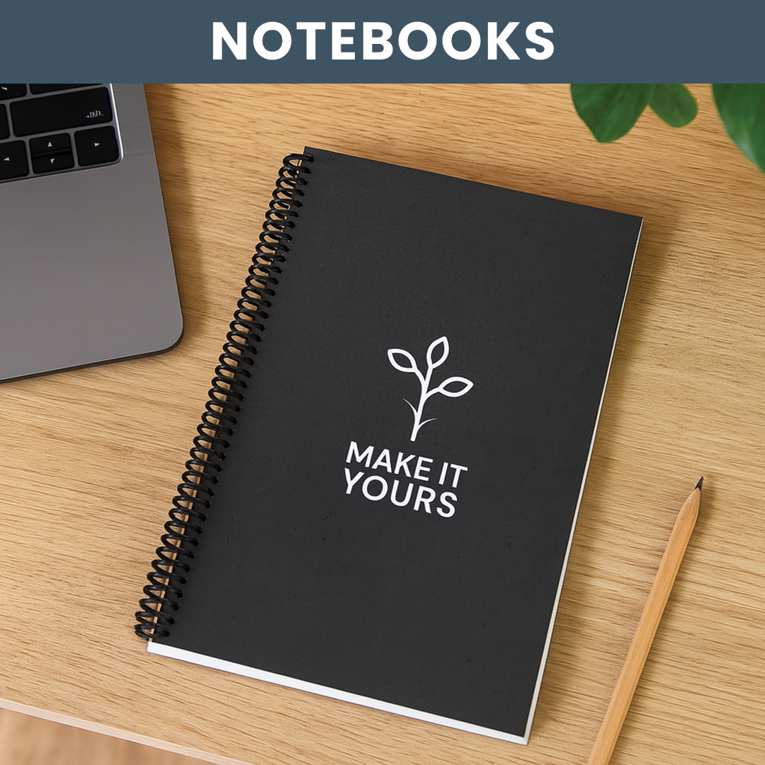 Lifestyle image of a notebook laying on a desk beside a plant, computer and a pencil